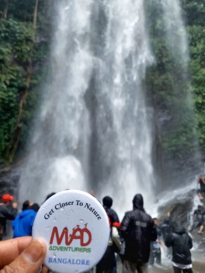 Our "Get Closer to Nature" badge held up against the backdrop of Hidlumane Falls, perfectly capturing our mission.