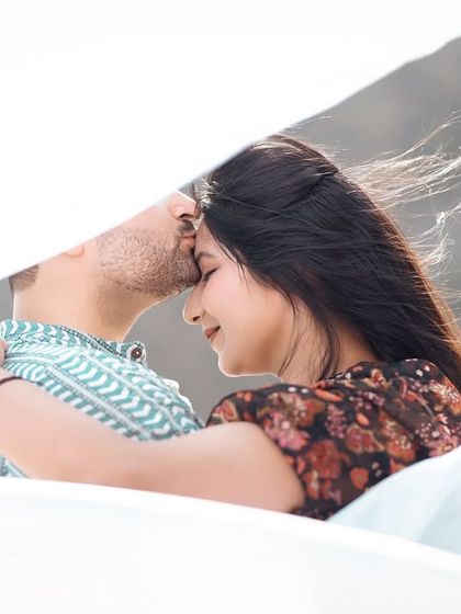 A gentle forehead kiss, with a soft white cloth creating a dreamy, veiled effect. This is a very intimate and artistic portrait.