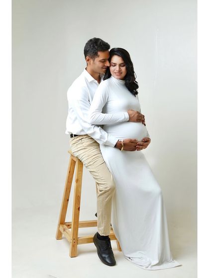 Using a simple prop like a stool can add variety to the poses. Here, the partner sits while embracing the mom-to-be, creating a stable and loving portrait.