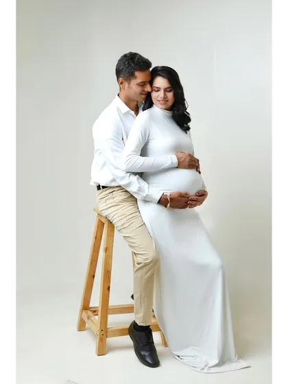 Using a simple prop like a stool can add variety to the poses. Here, the partner sits while embracing the mom-to-be, creating a stable and loving portrait.