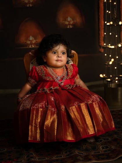 An adorable portrait of a toddler sitting gracefully in her festive red dress. The lighting highlights her innocent expression and the rich details of her outfit.