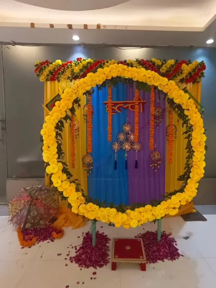 A colorful indoor Haldi setup with a large marigold ring. The backdrop uses blue, purple, and yellow drapes, creating a unique and vibrant setting for the ceremony.