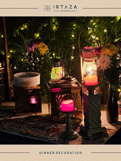 The dinner table decorated with glowing lanterns and fairy lights in the background, creating a magical and enchanting atmosphere for an evening event.