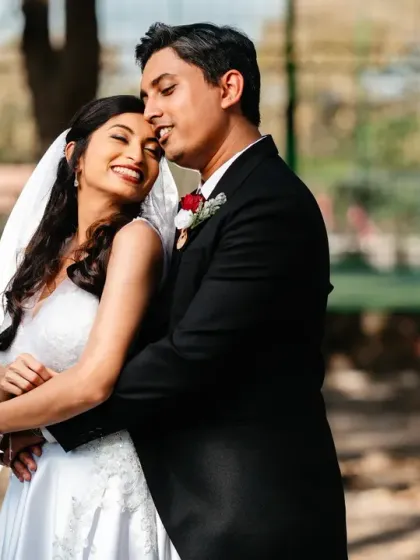 A warm, sun-drenched portrait filled with affection. The groom's gentle embrace and the bride's happy smile capture a perfect moment of quiet intimacy and happiness.
