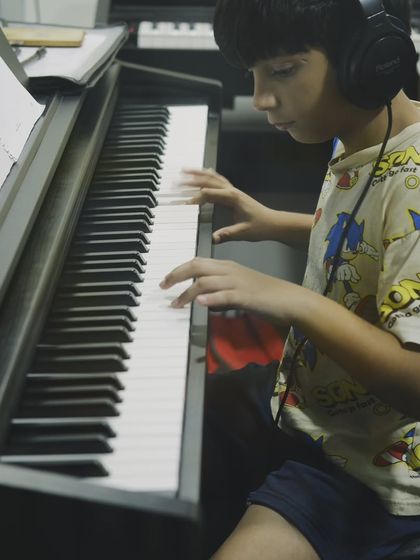 A student wearing headphones, completely focused on his piano practice. Providing individual headphones allows everyone in a group class to practice without distractions.