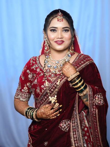 A classic bridal portrait in a rich red velvet saree. The makeup features a flawless base, traditional eye makeup, and is paired with heavy Kundan jewelry for a royal wedding look.