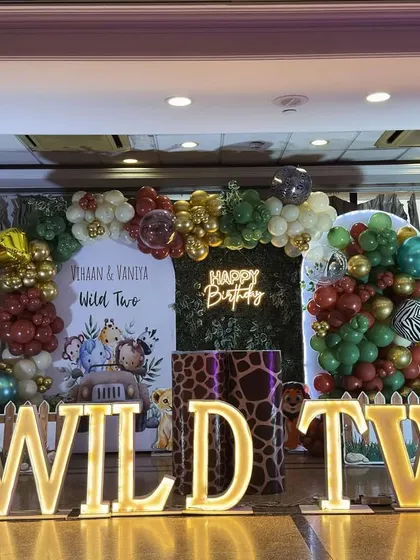 When the theme is "Wild Two," we go all out. This jungle safari setup for twins Vihaan and Vaniya features a lush green foliage backdrop, a custom balloon arch with animal print accents, and bold, illuminated "WILD TWO" marquee letters that set the stage for a roaring good time.
