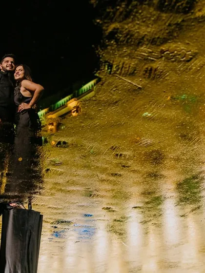 Using a puddle from the Mumbai monsoon, I created this artistic reflection shot. The couple stands against the dark night while the city lights paint a golden, abstract pattern on the water's surface.