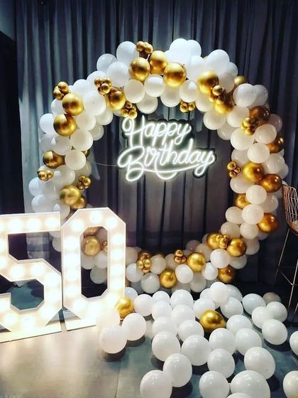 A classic and elegant setup for a 50th birthday, featuring a white and gold balloon ring, a neon sign, and large light-up marquee numbers.