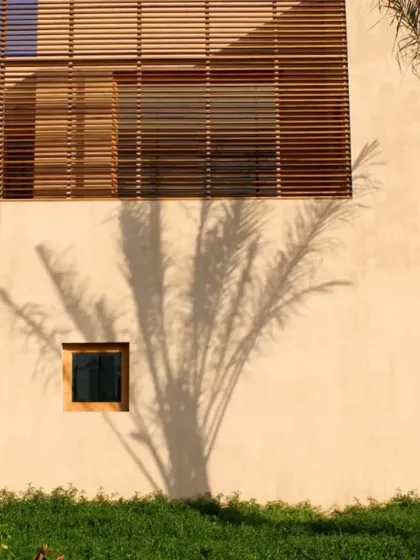 The shadow of a palm tree plays across the facade of the Sohar office. The wooden screen, or 'mashrabiya', is a modern interpretation of a traditional Islamic architectural element, providing privacy and shade while allowing ventilation.