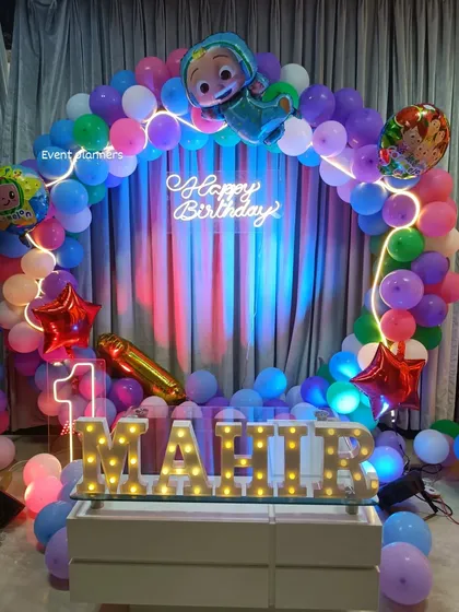 A Cocomelon-themed first birthday with a circular balloon arch and marquee letters.