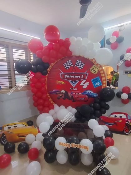 A Disney Cars themed birthday party with Lightning McQueen and Mater cutouts and a red, black, and white balloon arrangement.