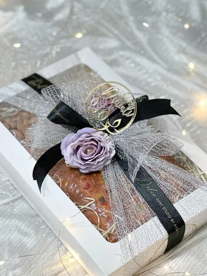 My Diwali box hamper is an elegant and simple gifting option. This beautifully wrapped box contains a large 500-gram tea cake along with jars of salted almonds and cashews. The lavender and black ribbon gives it a sophisticated touch.