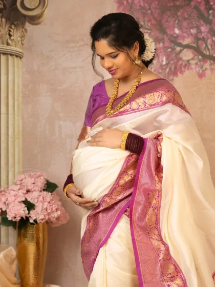 A close-up shot focusing on the mother's gentle connection with her baby. Her hands rest on her bump, and her serene expression is beautifully complemented by the traditional jewelry and flowers in her hair.