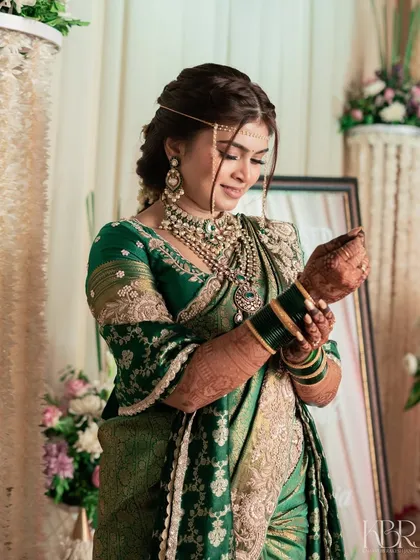 A candid shot of the bride adjusting her bangles. The makeup is flawless even in these unposed moments, with a focus on a clean, radiant complexion against her green silk saree.