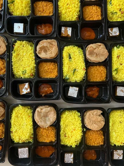 Simple Jain meal boxes prepared for a gathering of 60 people, featuring yellow rice and assorted vegetable dishes.