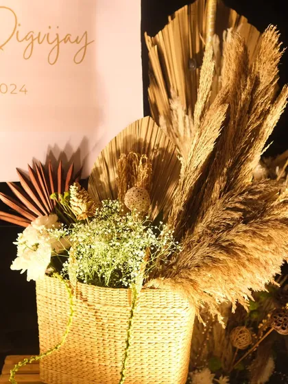 A detailed shot of a boho floral arrangement in a wicker basket. This piece combines dried pampas grass, palm leaves, and delicate white flowers for a beautifully textured and natural look.