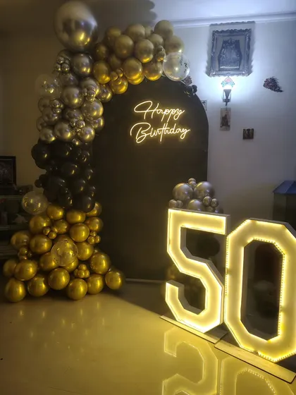 A classic black and gold theme for a 50th birthday celebration. The setup includes a half-arch of balloons on a black backdrop and a large light-up "50".