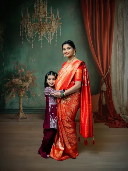 A beautiful moment between a mother and her daughter during a traditional maternity shoot. The mother's glowing presence in a red saree is complemented by her daughter's loving embrace.