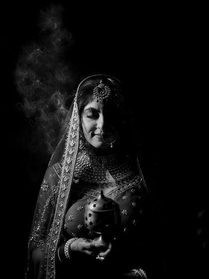 A black and white portrait of a bride holding an incense burner, her face partially in shadow.