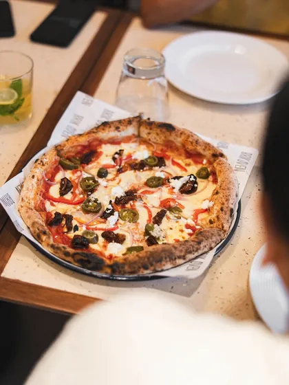 A full view of our pizza served at a table, ready to be sliced. The slightly blistered, airy crust and fresh toppings are a signature of our Neapolitan style.