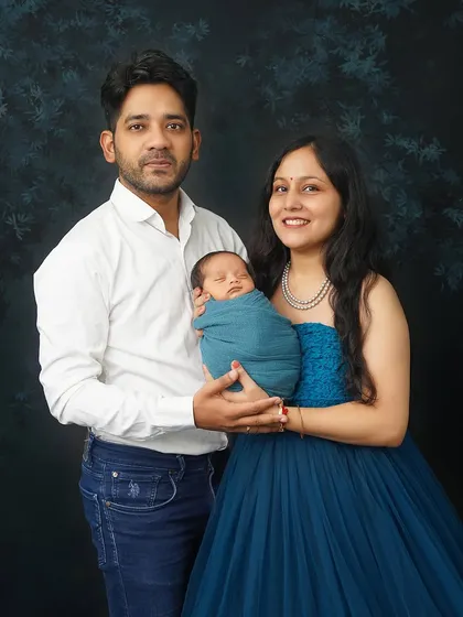 A classic family portrait with a newborn. The parents are dressed in elegant blue and white, holding their baby against a dark, moody backdrop for a timeless look.