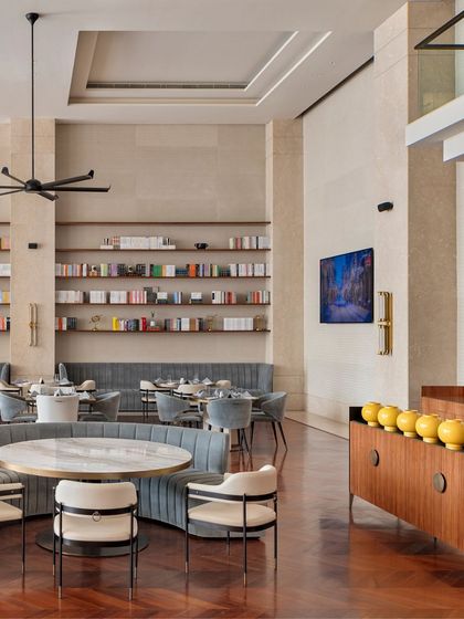 This wide shot of the Elevate Clubhouse dining room emphasizes the scale and elegance of the space. The high ceilings, extensive bookshelves, and refined furniture create an atmosphere of quiet luxury.