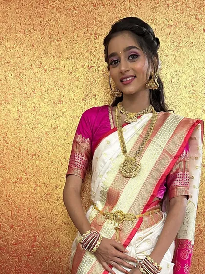 A full-length portrait of the bride, showcasing the complete look. The white and pink saree is a unique and beautiful choice for a wedding ceremony.