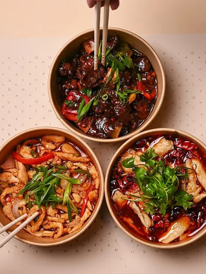 Two pairs of chopsticks dig into a trio of our hearty main courses. This image captures the social, sharing-style enjoyment of a Kaleido meal with friends or family.