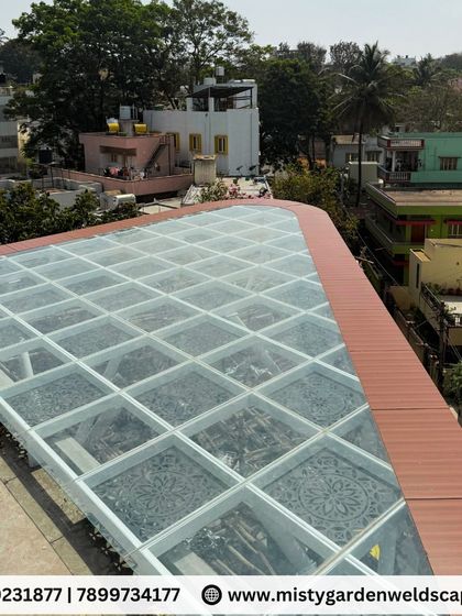 A high-angle view of the completed glass pergola roof. The clean grid of the frame and the alternating glass and CNC panels create a visually striking and highly functional structure.