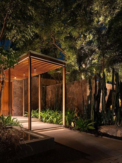 The entrance pathway to KEUS at night. The landscape lighting guides visitors while highlighting the textures of the stone walls, wooden canopy, and sculptural plants like cacti.