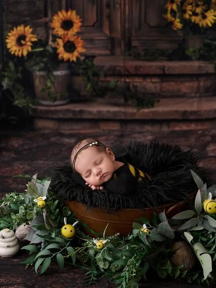 Our sweet little honey bee. A newborn sleeps in a "beehive" bucket surrounded by sunflowers, honey pots, and tiny bee decorations.