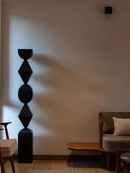 A play of light and shadow on a minimalist interior, highlighting a geometric black sculpture. The image captures the artistic and contemplative mood of the "In The Hills" sanctuary.
