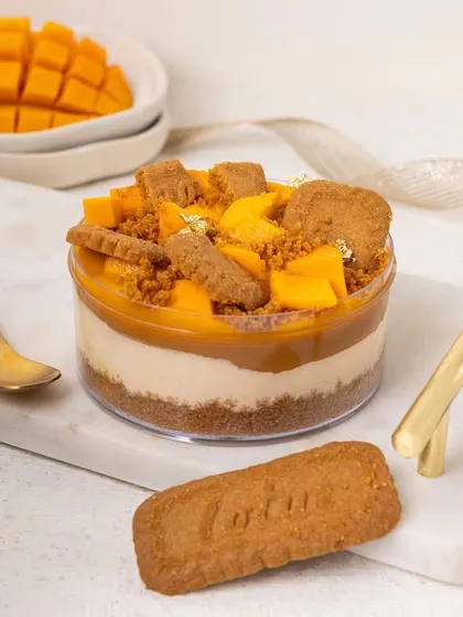 A tub of delicious mango and Biscoff cheesecake. The bright, high-key lighting and clean styling make this dessert look fresh, modern, and incredibly tempting.