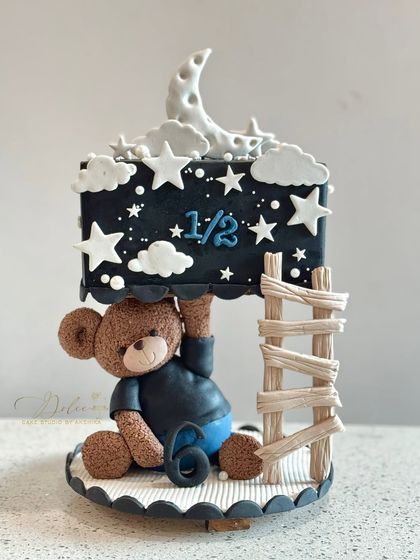 A half-birthday cake with a starry night theme. This design shows how to create a stable structure with a fondant teddy bear appearing to hold up the top tier.