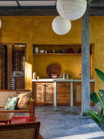 The living area of the private villa opens up to the plunge pool and surrounding greenery. The use of polished concrete floors, a warm yellow accent wall, and natural wood furniture creates a space that is both rustic and refined.