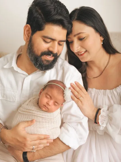 A close-up of a new family, with the baby sleeping peacefully on her father's chest while her mother looks on.