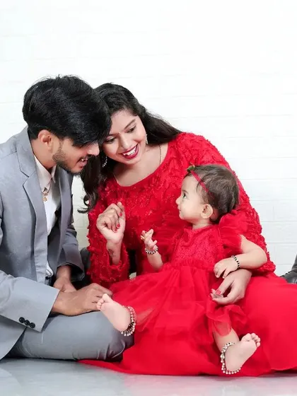 A sweet family moment on the floor, with everyone dressed in coordinating red and grey. The natural interaction and smiles make this a warm and authentic family portrait.
