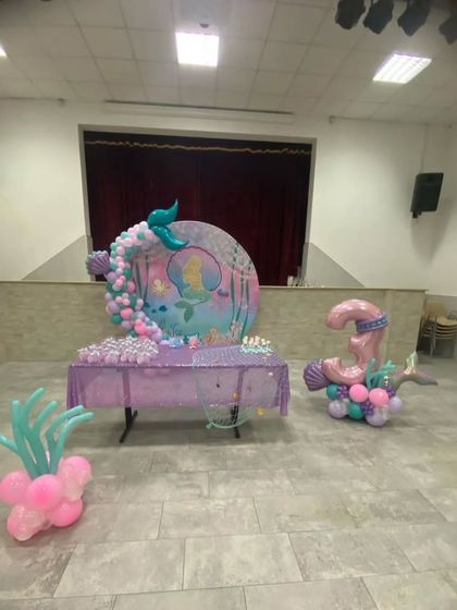 A mermaid-themed birthday party setup. This includes a custom table cover, a large number "3" balloon sculpture, and a backdrop with a mermaid silhouette, creating an underwater fantasy world.