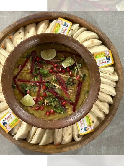 A deconstructed Chole Kulche platter. We serve the spicy chickpea curry in a traditional clay pot, surrounded by soft kulche bread, butter, and fresh lime, allowing everyone to assemble their own perfect bite.