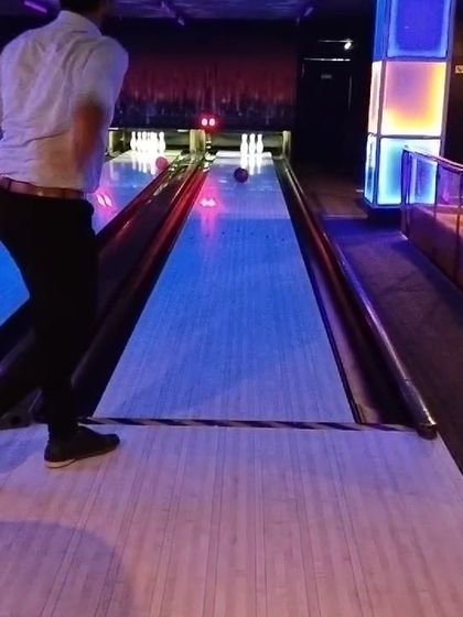 An action shot from our bowling league, capturing a player in mid-throw on our classic wooden lanes with colorful lighting.