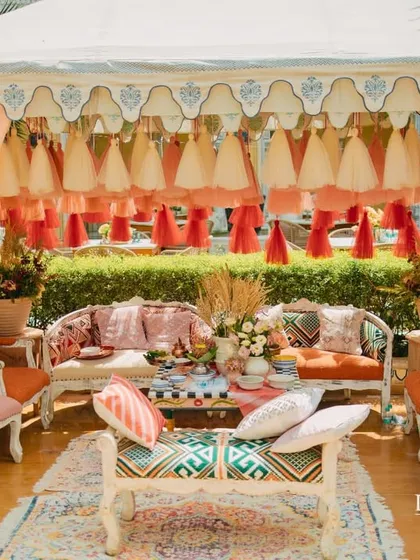 A regal Mehendi setup inside an embroidered tent. The custom furniture, printed textiles, and colorful tassels all contribute to a rich, layered, and luxurious atmosphere.