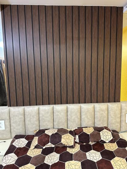 A stylish bedroom featuring a floor-to-ceiling upholstered headboard against a fluted wooden wall panel. This combination of soft and hard textures creates a cozy yet modern retreat.