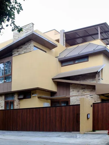 The home viewed from the street, nestled behind its wooden gate and surrounded by greenery, creating a private sanctuary within the city.