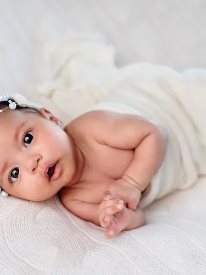 A beautiful shot of an awake newborn, wrapped gently and lying on a soft white blanket. Their curious expression is absolutely priceless.
