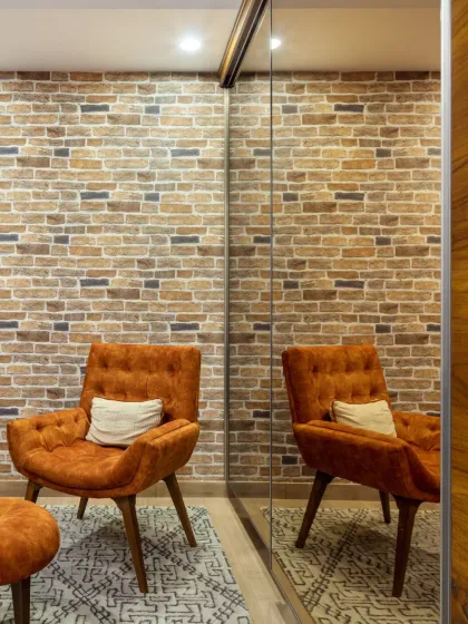 The clever use of a full-length mirror in the Rue 32 den creates an illusion of depth, making the compact space feel larger. The reflection of the exposed brick wall and the cozy orange lounge chair adds warmth and texture.