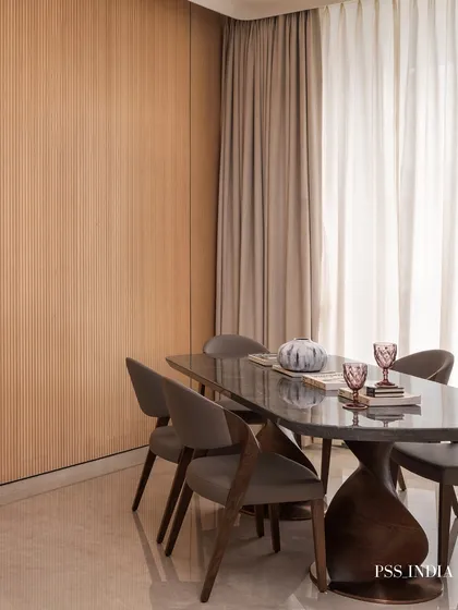 A modern dining setup featuring a sculptural table base and sleek grey chairs. The fluted wood wall and simple decor create a minimalist yet warm atmosphere.