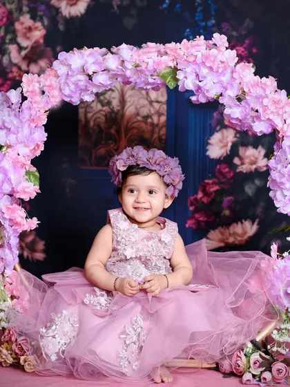 For this pre-birthday shoot, we created a dreamy floral wonderland. This little one is sitting on a beautiful swing adorned with pink and purple flowers, creating a magical portrait.