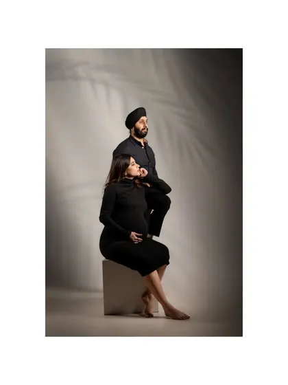 An editorial-style studio portrait of the couple. Their coordinated black outfits and posed, thoughtful expressions create a sophisticated and modern image.