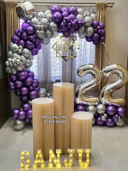 A stylish 22nd birthday setup at home. The purple and silver chrome balloon arch frames the window, creating a beautiful backdrop for photos.